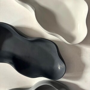 May include: Three ceramic bowls in different shades of gray. The bowls are all organic in shape with a wavy, asymmetrical rim.