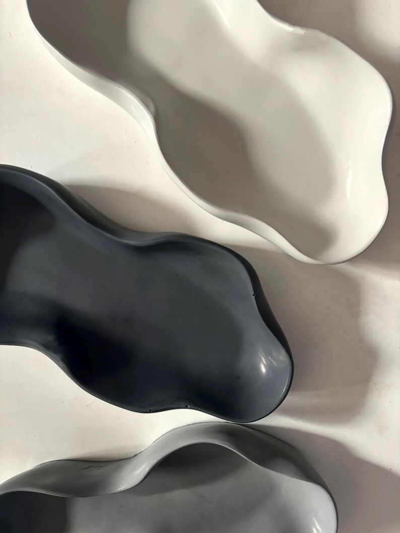 May include: Three ceramic bowls in different shades of gray. The bowls are all organic in shape with a wavy, asymmetrical rim.