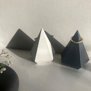 May include: Two geometric concrete ring holders, one white and one black, with a gold ring on the black holder.