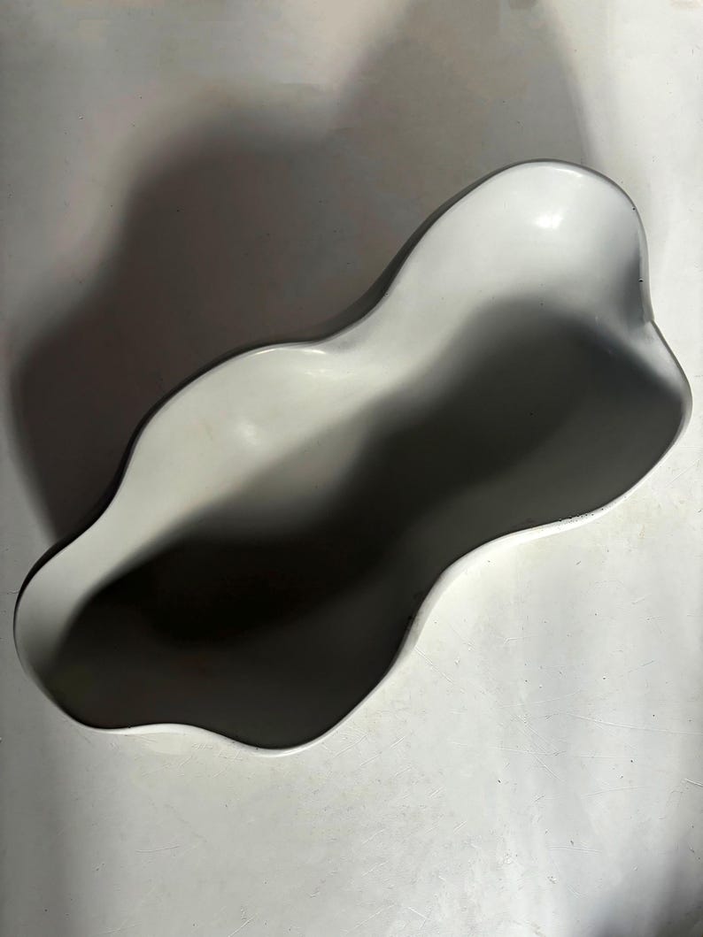 May include: A white ceramic planter with an organic, wavy shape. The planter is designed to hold plants or other decorative items.