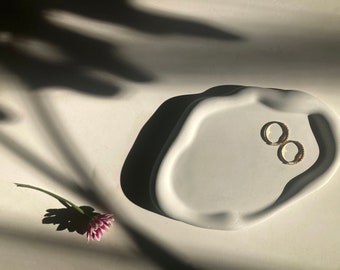 Peut inclure: Deux créoles en or avec de petites pierres claires serties dans le métal, reposant dans un plat en céramique blanche de forme irrégulière et organique.