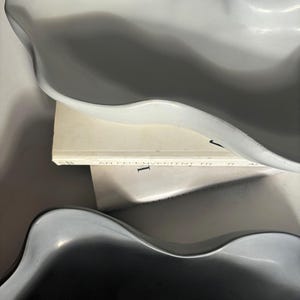 May include: Two ceramic bowls with a wavy, organic shape. The bowls are in shades of gray and white. The top bowl is white and the bottom bowl is a darker gray. The bowls are sitting on a white book with the text "An inconvenient truth" printed on the cover.