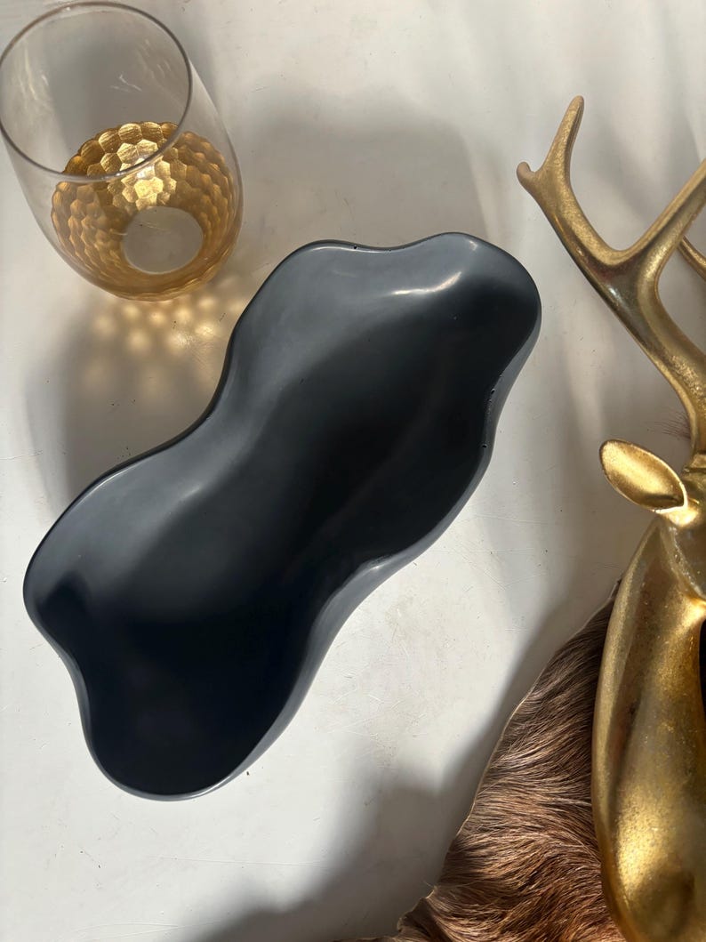 May include: A black, wavy, ceramic bowl with a smooth, glossy finish. The bowl is shaped like a long, narrow oval with a slight curve in the middle.