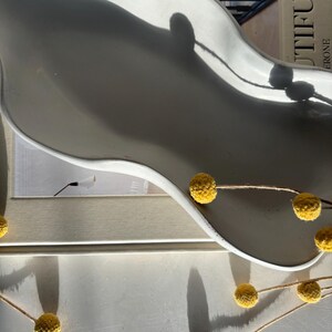 May include: White ceramic tray with a wavy edge, featuring a shadow of a window. The tray is decorated with a string of small yellow dried flowers.