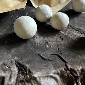 May include: A close-up of several small, white, round, smooth, clay balls on a dark brown wooden surface.