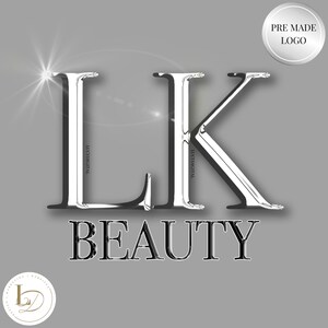 Puede incluir: Un logotipo metálico plateado con las letras "LK" en una fuente en negrita y estilizada. La palabra "BEAUTY" está escrita en negro debajo de las letras. El logotipo está sobre un fondo gris.