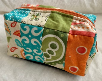 May include: A patchwork fabric zippered pouch with a variety of colours and patterns, including teal, green, orange, and white.