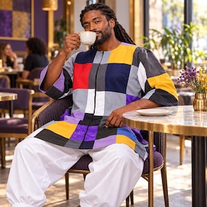 Puede incluir: Una túnica de manga larga con un vibrante diseño de patchwork multicolor con cuadrados rojos, amarillos, azules, morados, blancos y grises. La prenda tiene un cuello redondo, una cremallera vertical central y se combina con pantalones blancos holgados.