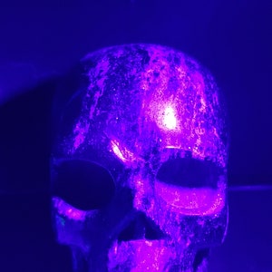 Puede incluir: Un cr&aacute;neo blanco con una superficie texturizada, iluminado con una luz p&uacute;rpura brillante.