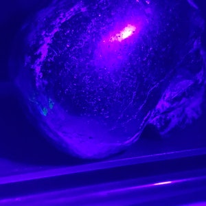 Puede incluir: Primer plano de un objeto redondo, texturizado, azul oscuro con una luz rosa brillante que lo atraviesa. El objeto est&aacute; sentado sobre una superficie que tambi&eacute;n est&aacute; iluminada con una luz rosa.