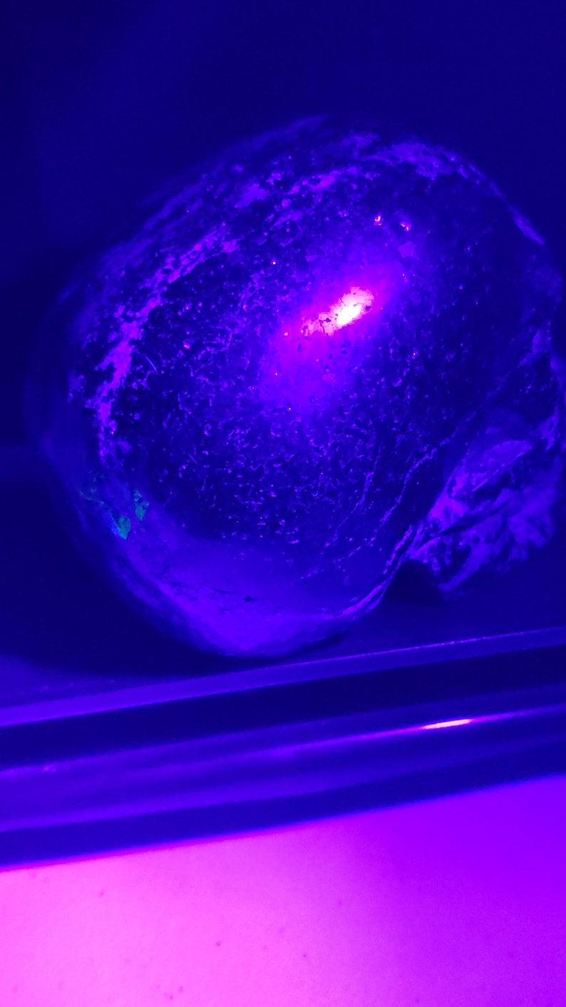 Puede incluir: Primer plano de un objeto redondo, texturizado, azul oscuro con una luz rosa brillante que lo atraviesa. El objeto est&aacute; sentado sobre una superficie que tambi&eacute;n est&aacute; iluminada con una luz rosa.