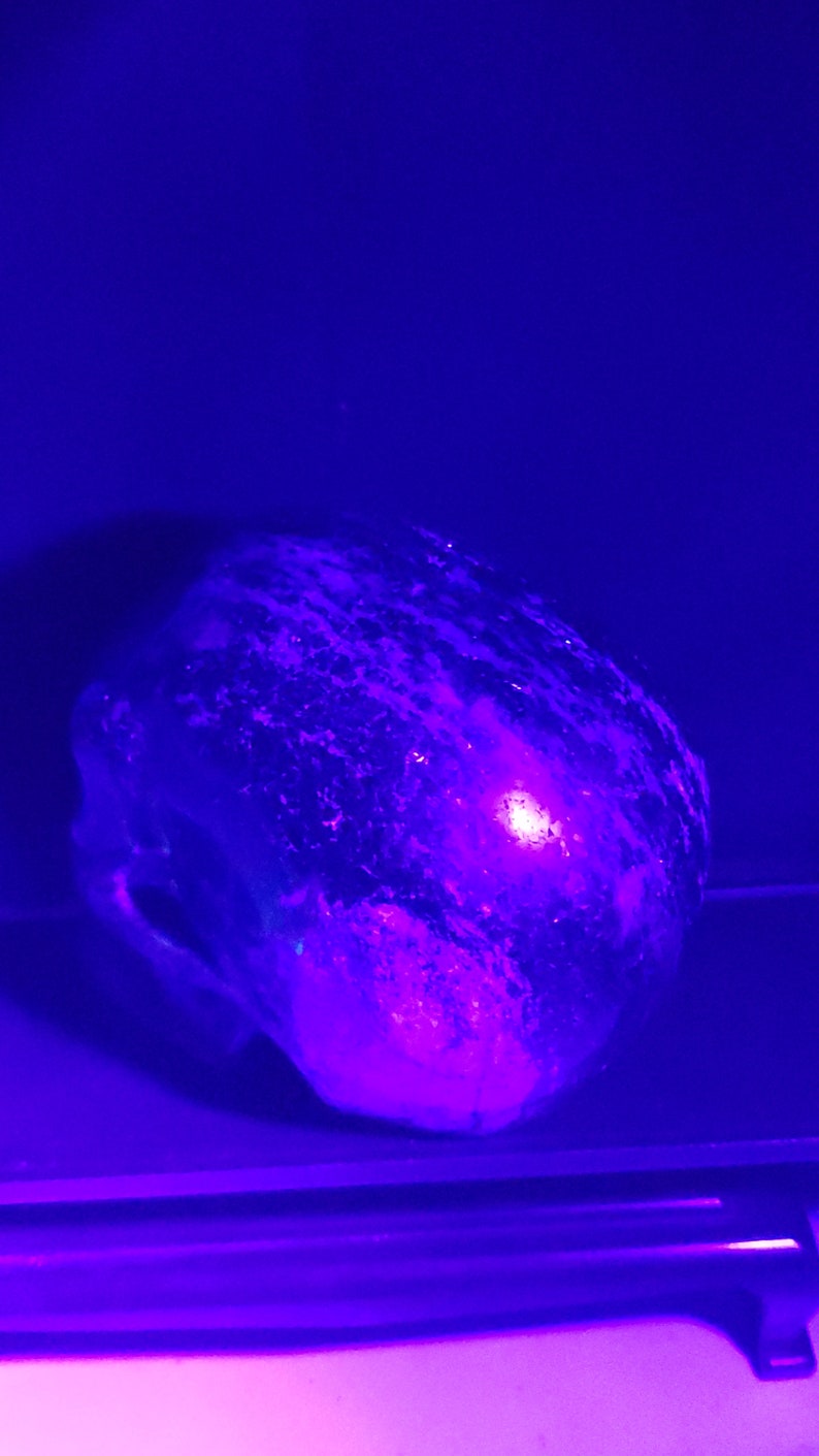 Puede incluir: Primer plano de una roca grande, redonda, de color p&uacute;rpura y negro con una superficie texturizada. La roca est&aacute; iluminada por una luz p&uacute;rpura brillante.