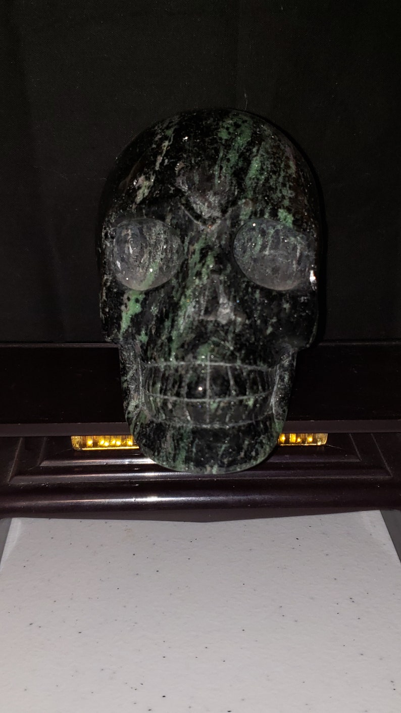 Puede incluir: Un cr&aacute;neo negro y verde hecho de piedra. El cr&aacute;neo tiene una talla detallada de los rasgos faciales y un patr&oacute;n de m&aacute;rmol verde y negro.