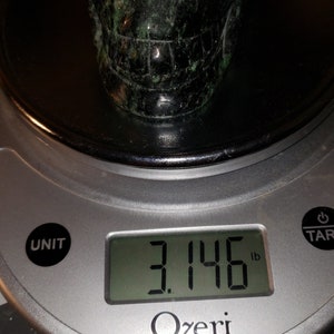 Puede incluir: Una escultura de piedra en forma de cr&aacute;neo de color verde y negro que pesa 3,146 libras en una b&aacute;scula digital.