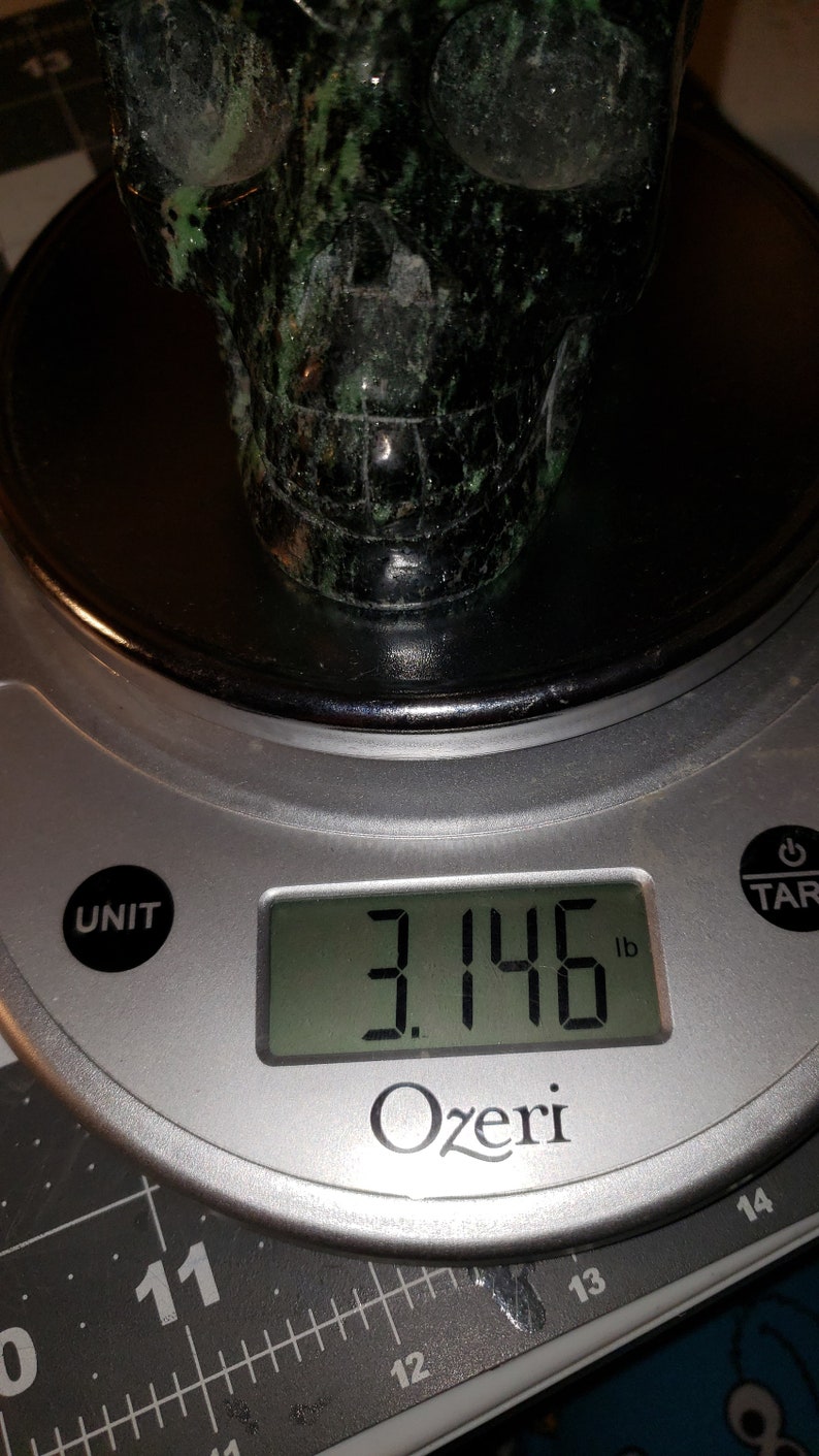 Puede incluir: Una escultura de piedra en forma de cr&aacute;neo de color verde y negro que pesa 3,146 libras en una b&aacute;scula digital.