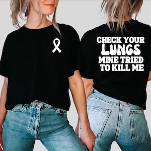Puede incluir: Dos camisetas negras con texto blanco. Una camiseta dice "Check Your Lungs Mine Tried To Kill Me" y la otra tiene una cinta blanca.