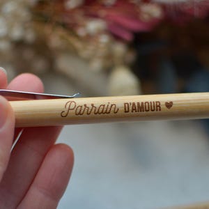 Op de afbeelding: Een houten pen met een zilveren clip en de woorden "Parrain D'Amour" erop gegraveerd. Een klein hartje is ook op de pen gegraveerd.