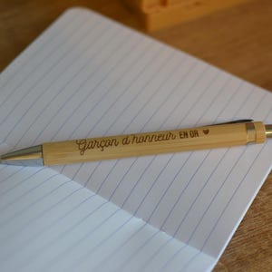Op de afbeelding: Een houten pen met de inscriptie "Gar&ccedil;on d'honneur en or" en een klein hartje.