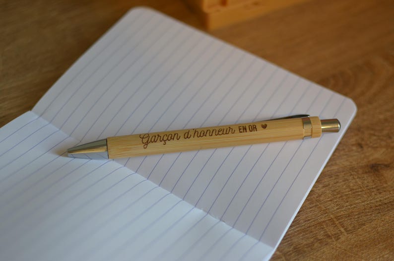Op de afbeelding: Een houten pen met de inscriptie "Gar&ccedil;on d'honneur en or" en een klein hartje.