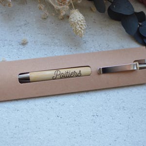 Op de afbeelding: Een bruine kartonnen penhouder met een houten pen waarop het woord "Poitiers" is gegraveerd.