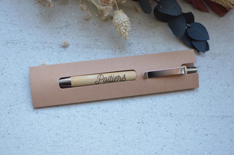 Op de afbeelding: Een bruine kartonnen penhouder met een houten pen waarop het woord "Poitiers" is gegraveerd.