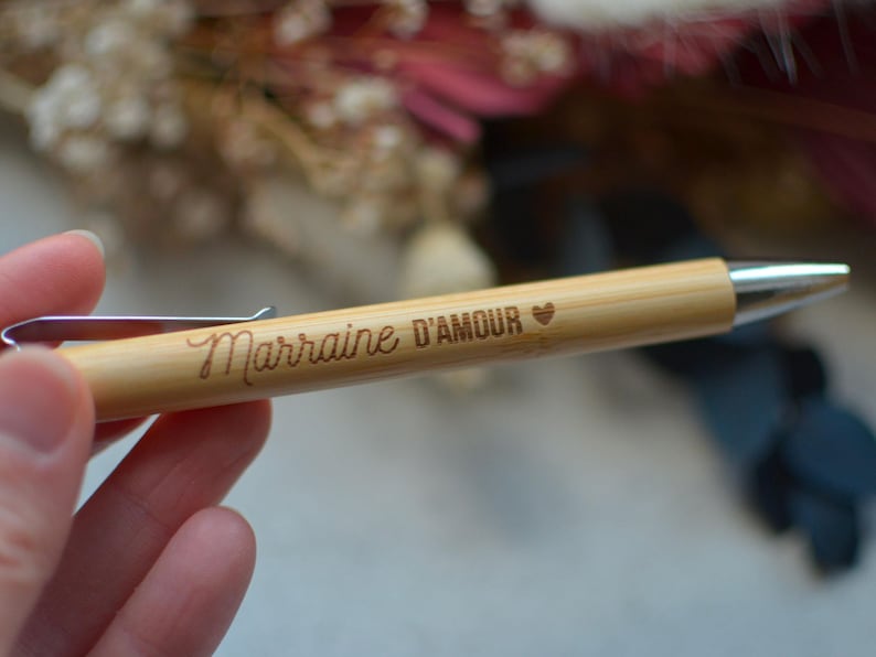 Op de afbeelding: Een houten pen met een zilveren clip en een zilveren punt. De pen is gegraveerd met de woorden "Marraine D'Amour" en een klein hartje.