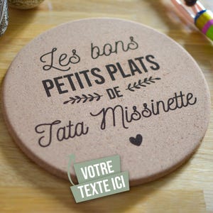 Peut inclure: Sous-plat en liège avec le texte "Les bons petits plats de Tata Missinette" et un cœur. Le sous-plat a un espace pour "Votre texte ici".