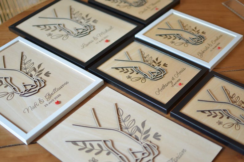 Puede incluir: Obras de arte de madera cortadas con l&aacute;ser que presentan manos entrelazadas, detalles florales y texto personalizado, enmarcadas en blanco y negro. Ideal para regalos de boda o aniversario.