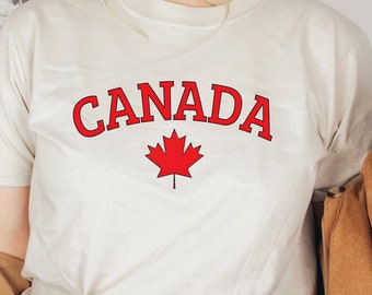 May include: White t-shirt with red text that says "CANADA" and a red maple leaf graphic.