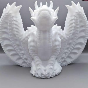 Może przedstawiać: Biała ceramiczna figurka smoka z rozłożonymi skrzydłami. Smok ma szczegółową, fakturowaną powierzchnię i lekko otwarte usta.