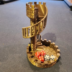 Può includere: Una torre dorata stampata in 3D con una scala a chiocciola e una base che contiene dadi. La torre è su una superficie di feltro verde.