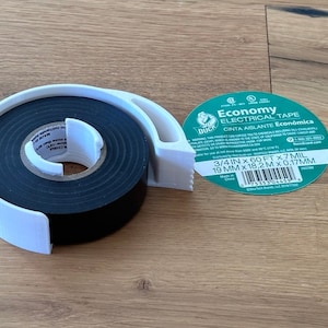 May include: A roll of black electrical tape in a white dispenser with a label that reads "Economy Electrical Tape" and "3/4 in x 60 ft x 7 mil 19 mm x 18.2 m x 0.17 mm".