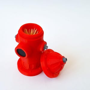 May include: A bright red fire hydrant-shaped toothpick holder with a removable lid. The holder is filled with wooden toothpicks. The lid is next to the holder. The holder has gray accents and a black circle.