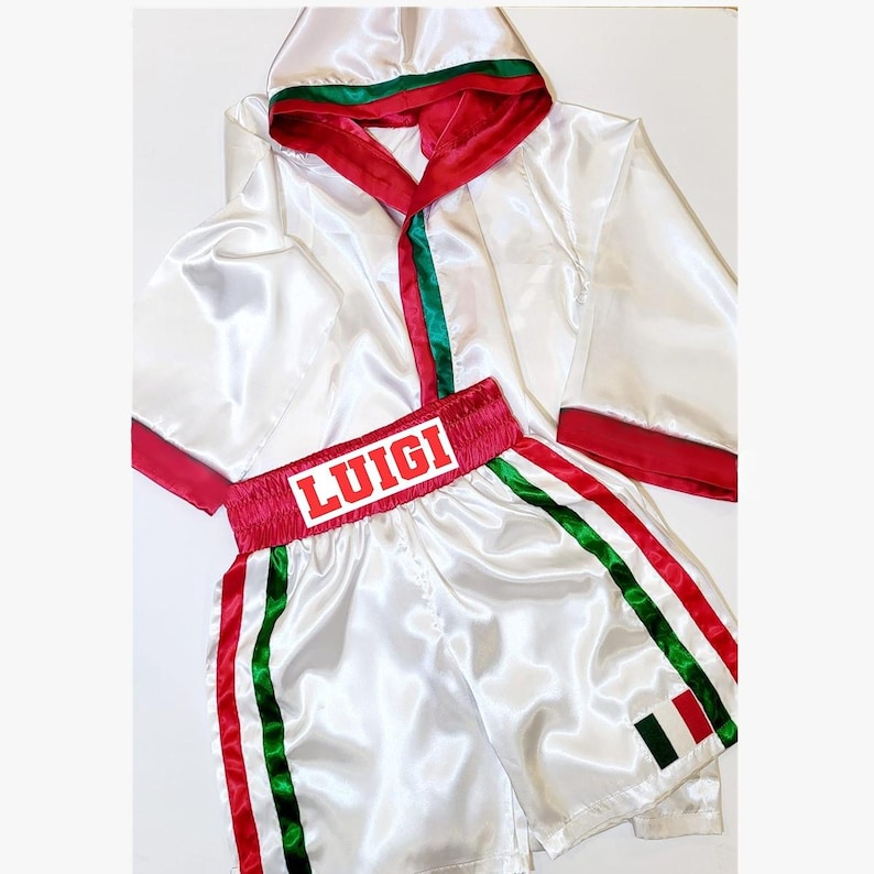 Peut inclure: Ensemble de boxe en satin blanc. La robe a une bordure rouge et verte sur la capuche et les manches. Le short porte le nom "LUIGI" en lettres rouges sur la ceinture et des rayures vertes et rouges sur les c&ocirc;t&eacute;s. Un drapeau italien est sur le short.