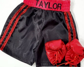 May include: Black satin boxing shorts with red glitter trim and the name "TAYLOR" embroidered on the waistband. The shorts are paired with two red glitter boxing gloves.