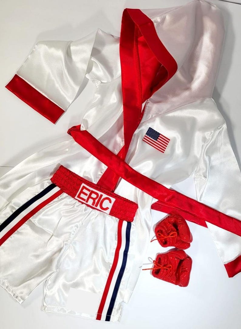 May include: White satin boxing robe with red trim and a red sash. The robe has an American flag patch on the chest.  White satin boxing shorts with red and blue trim. The shorts have the name "ERIC" on the waistband.  A pair of red boxing gloves.