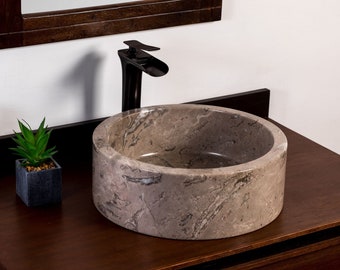 May include: A round, light brown stone vessel sink with a black faucet. The sink is on a dark brown wooden countertop.