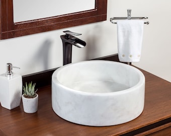May include: White marble vessel sink with a black faucet and a white towel hanging on a chrome towel rack.