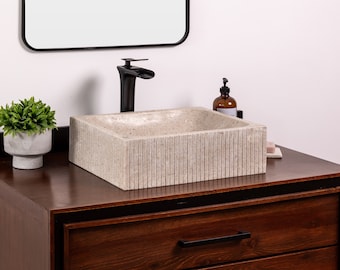 May include: A white stone vessel sink with a rectangular shape and a textured, ribbed exterior. The sink is mounted on a dark brown wooden vanity with a black drawer pull.