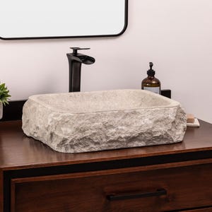 May include: A white stone vessel sink with a rough, textured exterior sits on a dark wood countertop. A black faucet is mounted above the sink.