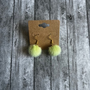 May include: A pair of green fuzzy pom-pom earrings with gold hooks.