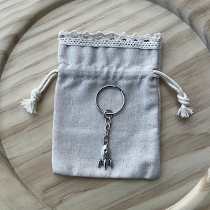May include: A small, white drawstring bag with a silver rocket ship keychain. The bag has a lace trim and is tied with a string.