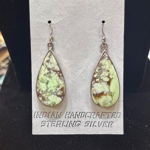 May include: Teardrop earrings featuring a light green and brown stone, set in sterling silver. The earrings are displayed on a grey card with the text "INDIAN HANDCRAFTED STERLING SILVER".