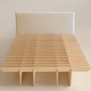 May include: A modern bed frame with a light-colored wooden slatted base and a rectangular, off-white upholstered headboard. The bed frame is constructed with vertical supports and horizontal slats, creating a minimalist design.