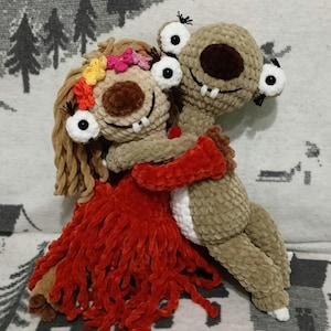 Könnte beinhalten: Zwei gehäkelte Plüschtiere, eines braun mit langem Hals und großen Augen, das andere braun mit einem roten Kleid und einer Blumenkrone, umarmen sich.