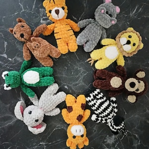 May include: A collection of ten crocheted stuffed animals in various colors and animal designs, including a tiger, lion, frog, zebra, giraffe, and bunny. The animals are arranged in a circle on a dark gray surface.
