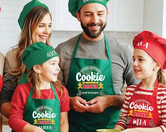 May include: A family of four wearing green and red Christmas-themed aprons with the text "Official Christmas Cookie Baker" and their names. The aprons have a gingerbread man design and holly leaves.