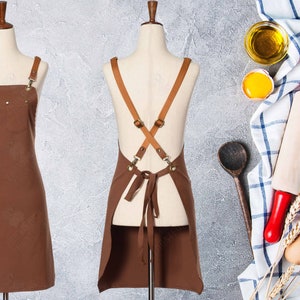 May include: Brown leather-strapped apron with a large pocket on the front. The apron is on a white mannequin.