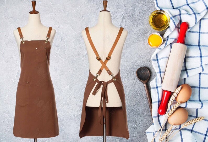 May include: Brown leather-strapped apron with a large pocket on the front. The apron is on a white mannequin.