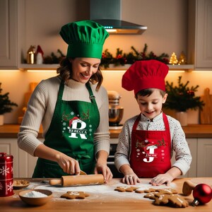 May include: A woman and a child wearing green and red Christmas-themed aprons with reindeer and Santa hats. The aprons are personalized with the letters "R" and "J" and the names "Rebecca" and "Jacob". They are baking cookies in a kitchen.